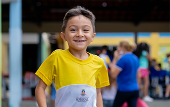 Um menino de camiseta amarela está sorrindo com motivação.