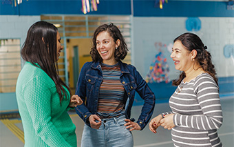 Três mulheres envolvidas em discussões socioemocionais no corredor de uma escola.