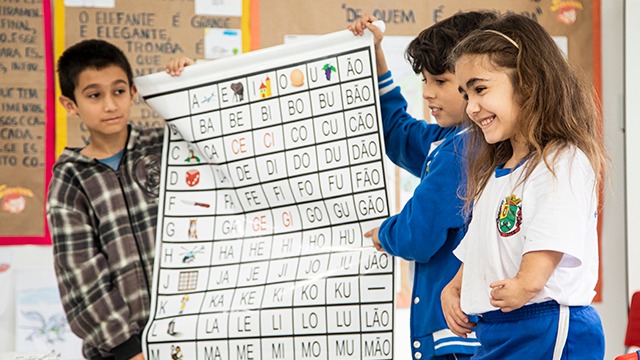 Na Sala De Aula, um grupo de crianças ao lado de um quadro com números.