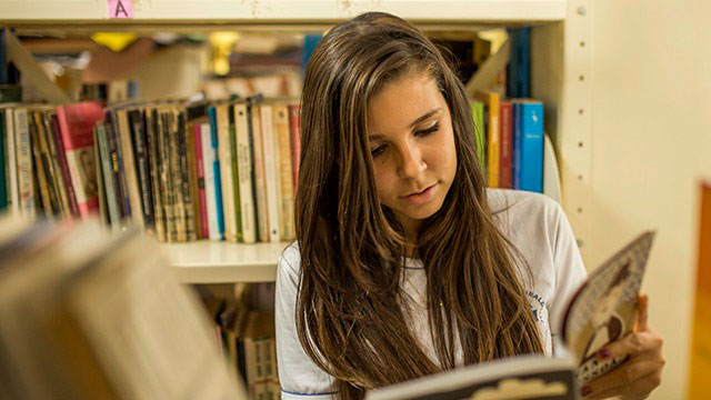 Na Sala De Aula, uma menina lendo um livro em uma biblioteca.