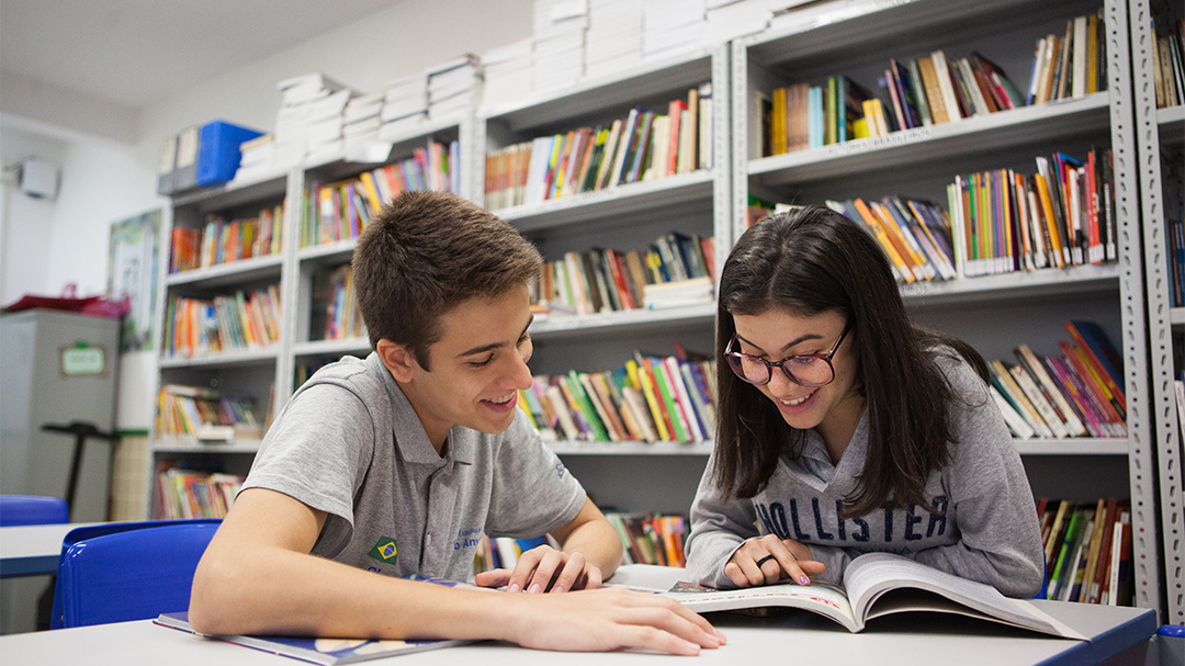 Um menino e uma menina conduzindo uma pesquisa sobre o mundo do trabalho em uma mesa de uma biblioteca.