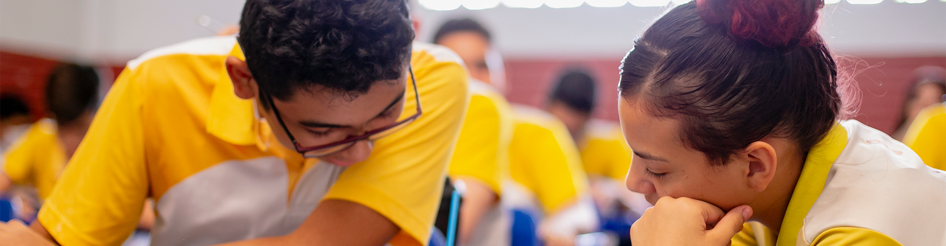 Um grupo de pessoas de camisa amarela participa de diálogos socioemocionais dentro de uma sala de aula.