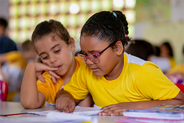 Acelera Brasil - Duas meninas sentadas à mesa de uma sala de aula.