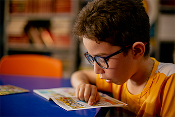 Um menino, imerso no mundo da “Se Liga”, lê uma revista em quadrinhos em um canto tranquilo da biblioteca.