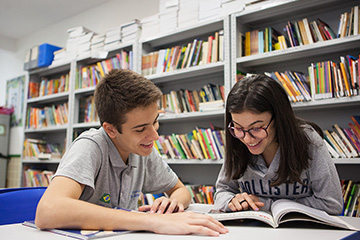 Um menino e uma menina pesquisam sobre o Mundo do Trabalho em uma mesa de uma biblioteca.