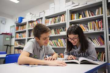 Dois alunos estudando em uma biblioteca com estantes, com foco em Educação Integral para o Ensino Médio (RJ).