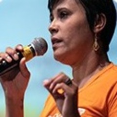Uma mulher chamada Verônica Santos, vestindo uma camisa laranja, falando ao microfone.