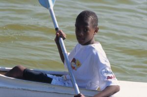 Um menino em uma canoa branca vivenciando a Educação pelo Esporte.