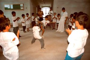 Grupo de crianças participantes do programa Educação pelo Esporte, vestindo camisas brancas, brincando em uma sala.