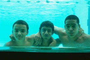 Três jovens participantes do programa Educação pelo Esporte, posando debaixo d'água em uma piscina.