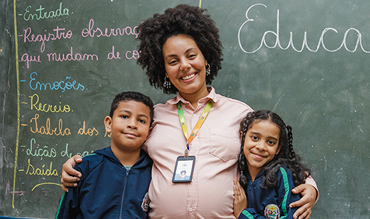 A pregnant woman and children standing in front of a chalkboard, advocating for education.