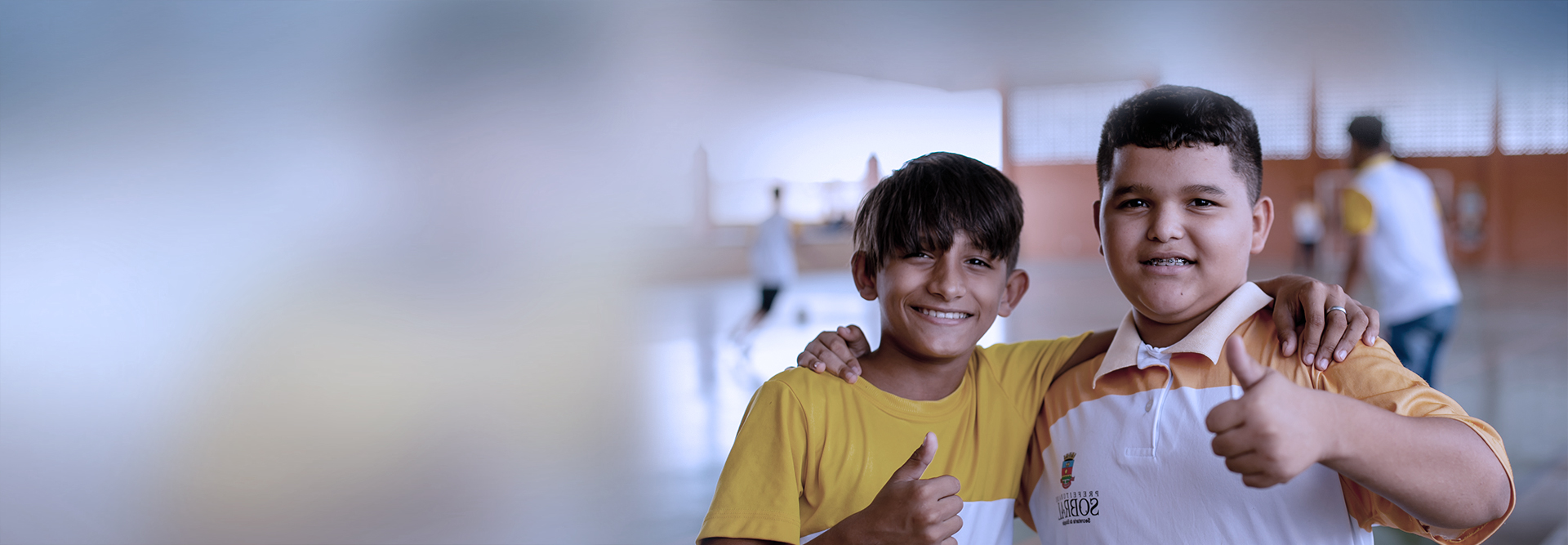 Two boys giving thumbs up in a gym, supporting education.