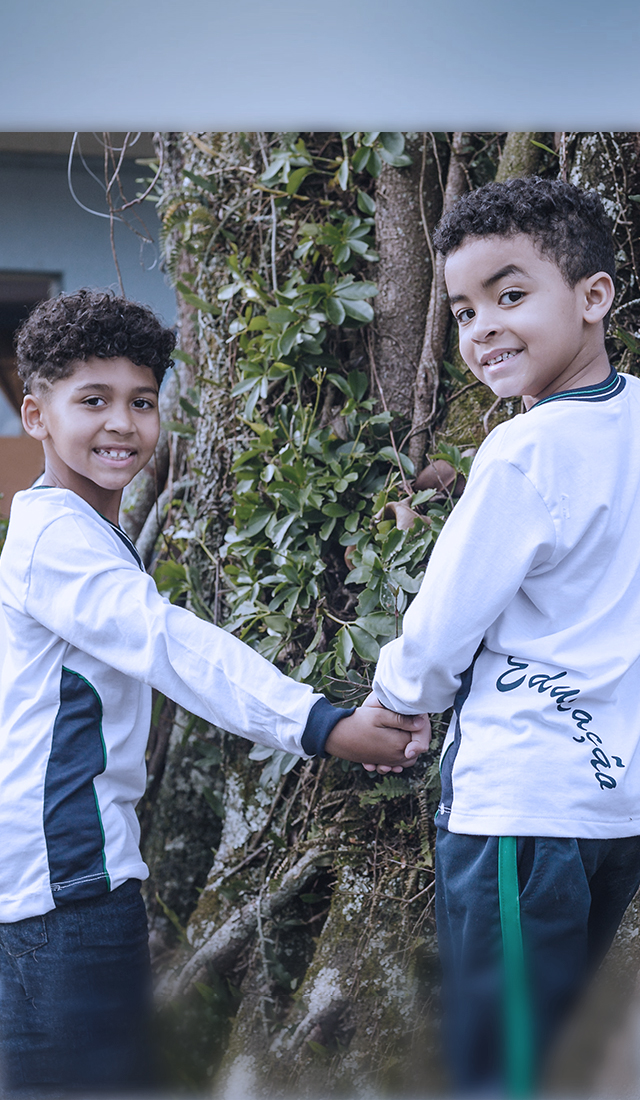 Dois meninos de mãos dadas em frente a uma árvore, apoiando o Instituto Ayrton Senna e a educação.