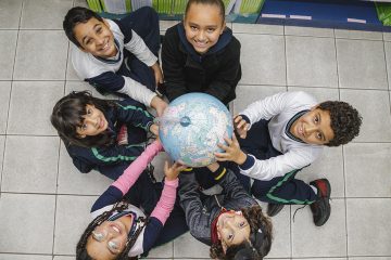 Grupo de crianças segurando um globo, com destaque para a parceria com o Instituto Ayrton Senna.