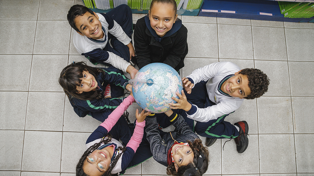 A group of children holding a globe as part of the Company Donation initiative in partnership with the Ayrton Senna Institute.