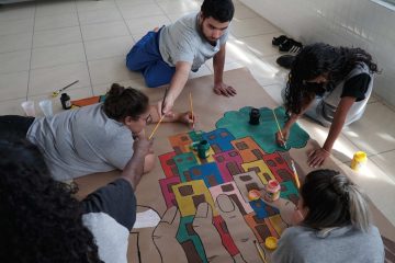 Grupo de pessoas trabalhando em desenho colaborativo no chão para promover a educação em São Luís (MA) e beneficiar 7 mil alunos de escolas municipais.