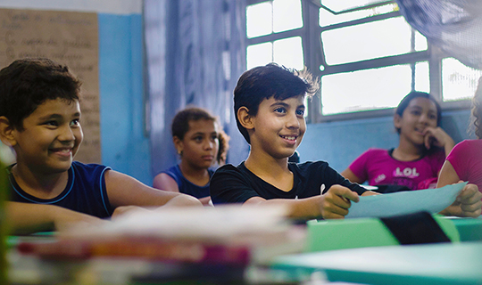 Um grupo de crianças sentadas em carteiras em uma sala de aula demonstra seu apoio à educação ao apoiar a Apoie a educação, campanha do Instituto Ayrton Senna.