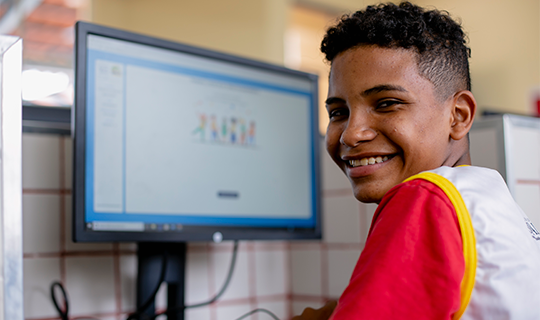 Um menino sorrindo enquanto usa um computador para Conteúdos para comunicador.