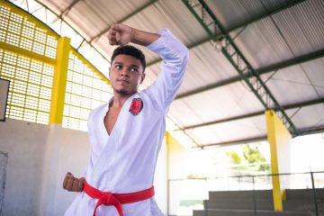 Um jovem com uniforme de caratê vermelho e branco praticando Educação pelo Esporte.