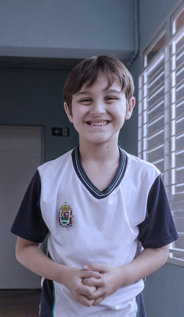 Um menino com uniforme escolar sorrindo, apresentando conteúdos para comunicador.