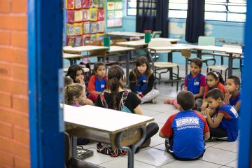Um grupo de crianças sentadas em círculo na sala de aula, participando de iniciativas educacionais inovadoras no século XXI.