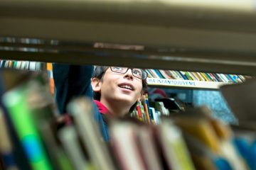 Um menino está olhando uma estante de livros.