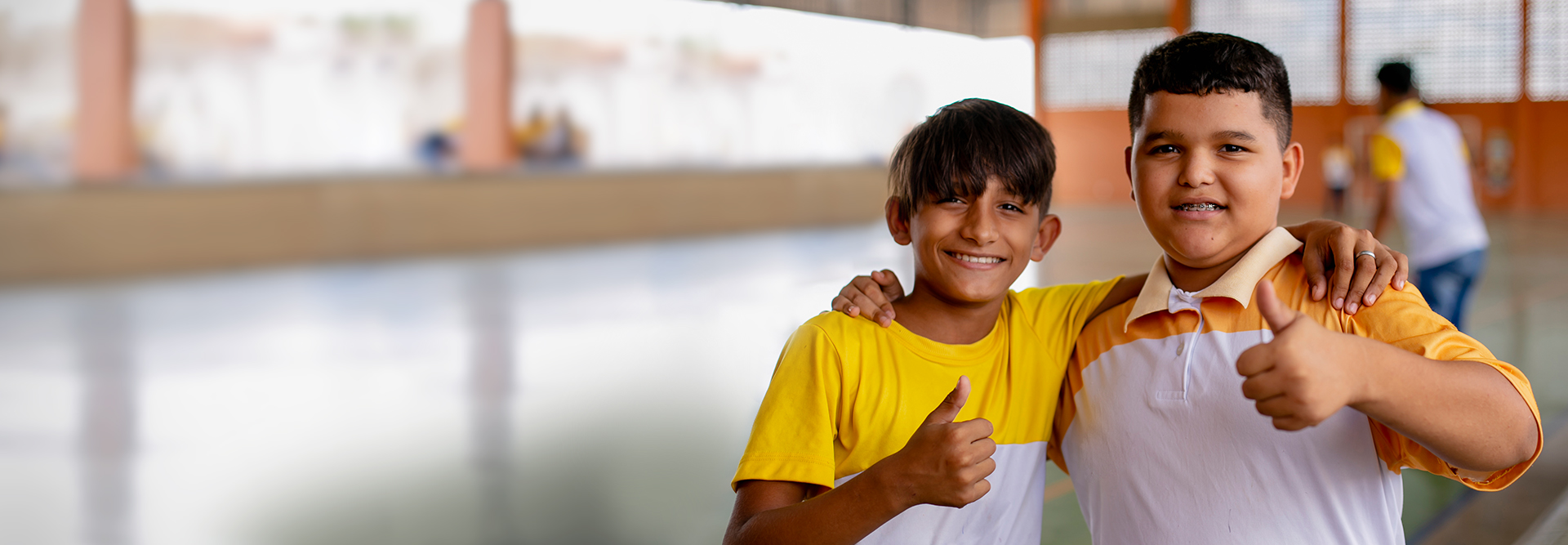 Dois meninos fazendo sinal de positivo em um ginásio, incentivando os espectadores a doarem para a educação.