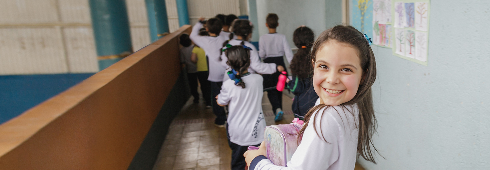 Um grupo de crianças em um corredor com a foto de uma menina, rodeadas de Componentes Educacionais.