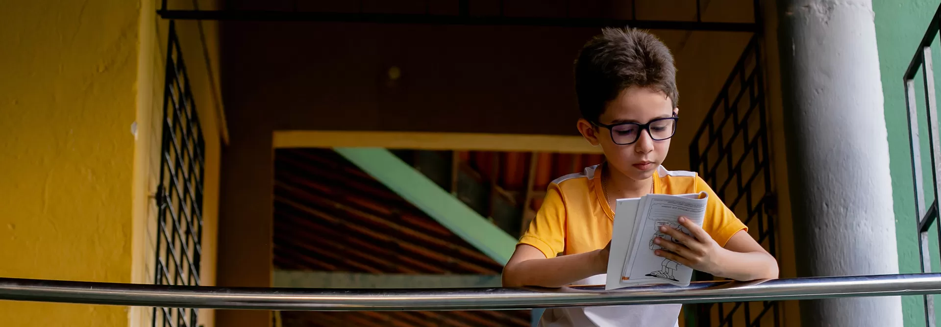O Que Fazemos: Um menino está lendo um livro em uma grade.