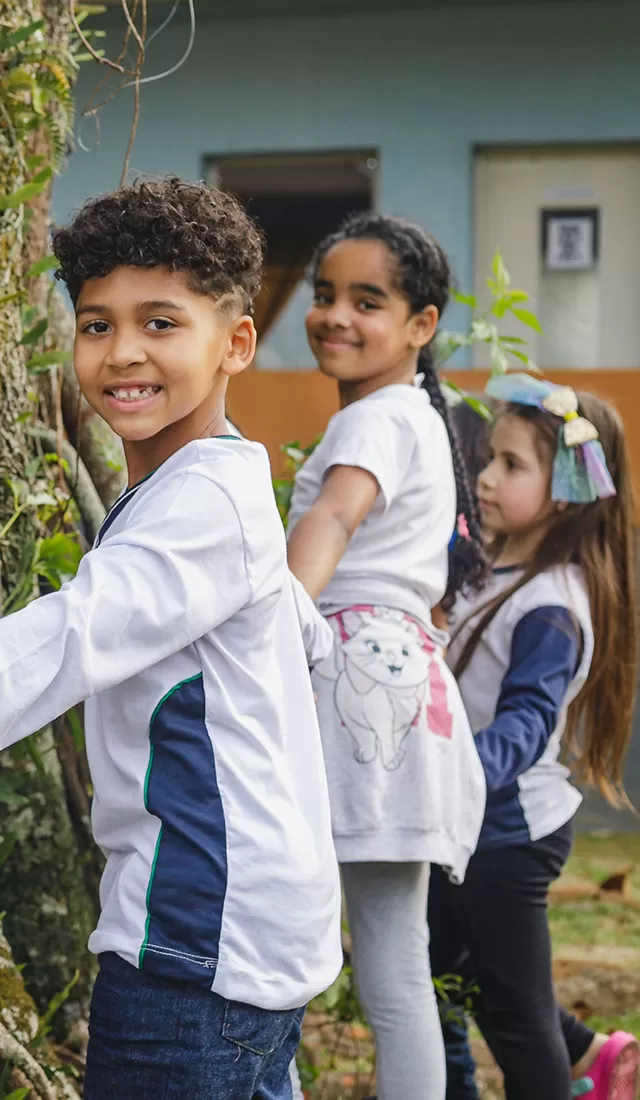 Um grupo de crianças planta uma árvore no pátio de uma escola, apoiando a missão do Instituto Ayrton Senna de promover a educação.