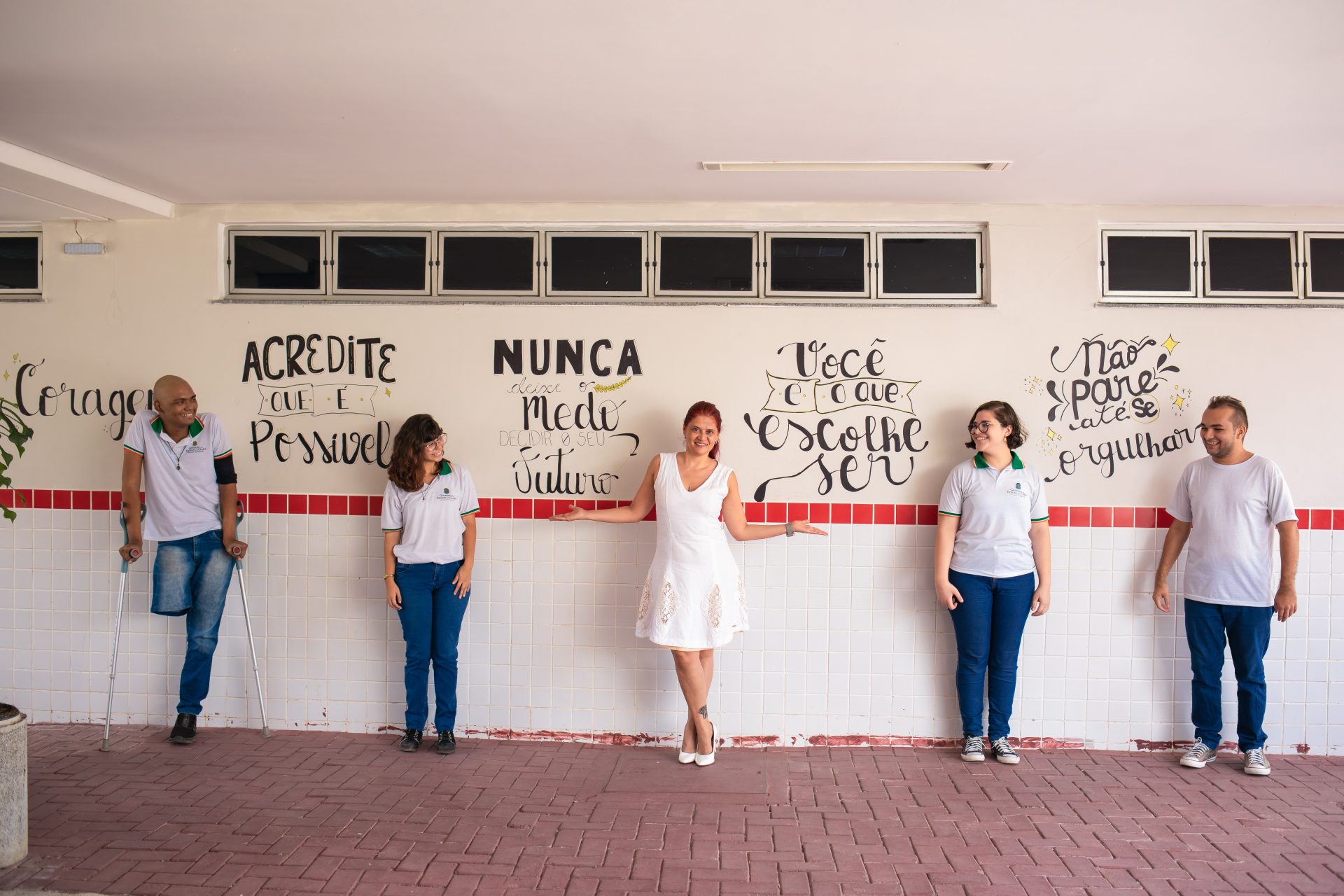 Quatro adolescentes e uma mulher adulta diante de um mural com as frases: Coragem, acredite que é possível, nunca deixe o medo decidir o seu futuro, você é que escolher ser, não pare até se orgulhar