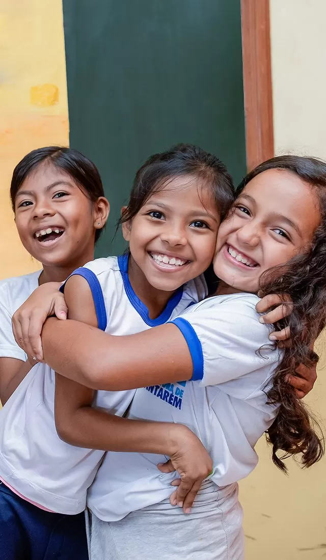 Alunas se abraçam e brincam sorridentes na sala de aula