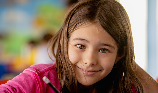 Menina aluna sorrindo na sala de aula com lápis na mão