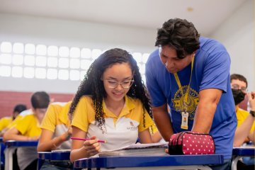Uma estudante sendo ensinada por um professor em uma escola fortalecida por empresas que acreditam na educação brasileira.