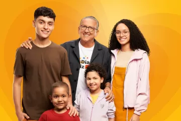 Galvão Bueno, estudantes e duas crianças posam diante de um fundo laranja como parte da iniciativa McDia Feliz 2023.