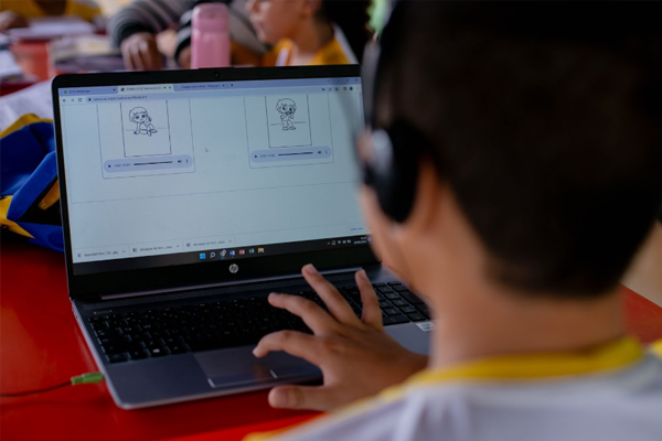 Um menino está usando um laptop em uma sala de aula para alfabetização.
