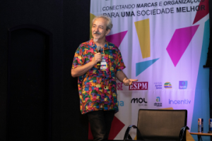 Wellington Nogueira (Doutores da Alegria) segurando apaixonadamente um microfone, dirigindo-se ao público durante o encerramento do Fórum Marketing de Causa 2023.
