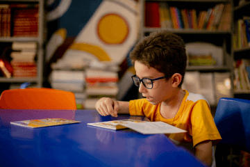 Um menino lendo um livro em uma biblioteca.