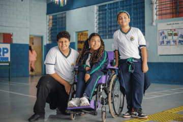 Três crianças em cadeira de rodas posam para foto.