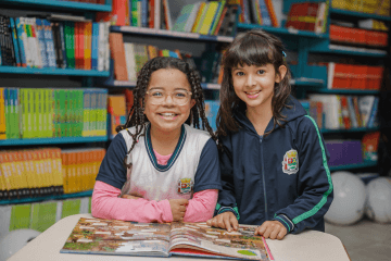 Duas meninas sorrindo para um livro em uma biblioteca.