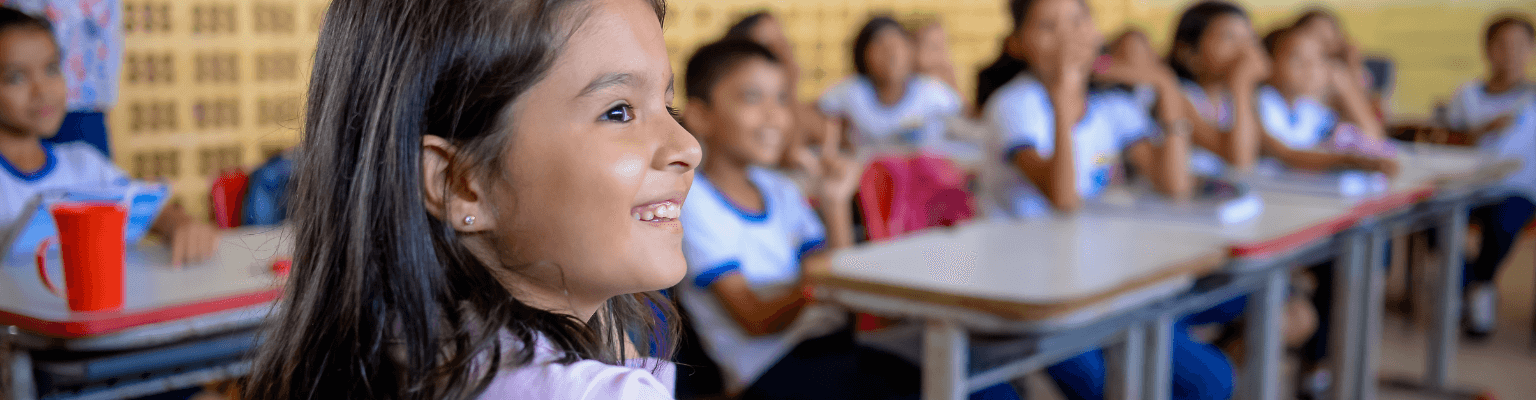 Um grupo de crianças sentadas em carteiras em uma sala de aula engajadas na alfabetização.