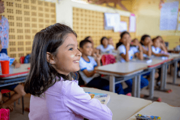 Uma jovem sentada à mesa de uma sala de aula, focada nos estudos de alfabetização.