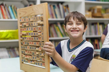 Um menino segura uma tábua de madeira em uma sala de aula, demonstrando a importância de compreender a criatividade das crianças.