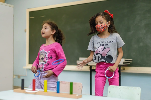 Duas meninas brincando com brinquedos em uma sala de aula, explorando a criatividade infantil e compreendendo sua importância para o desenvolvimento.