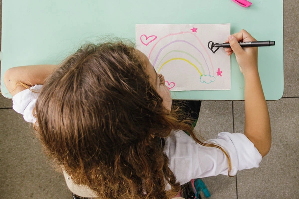 Uma garota expressa sua criatividade desenhando um arco-íris em um pedaço de papel.