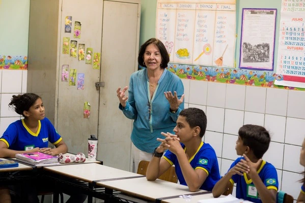 Uma mulher está ensinando uma turma de crianças em uma sala de aula, oferecendo educação por meio do sistema educacional brasileiro.