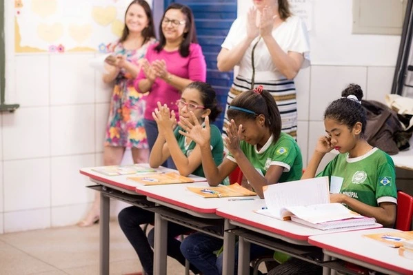 Um grupo de crianças batendo palmas em carteiras em uma sala de aula enquanto desenvolvem habilidades socioemocionais.