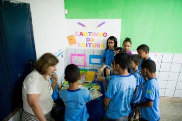 Um grupo de crianças com camisas azuis em volta de uma mesa realiza atividades para desenvolver habilidades socioemocionais.