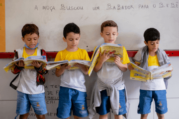 Um grupo de crianças lendo livros em uma sala de aula.