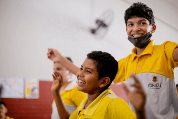 Dois meninos de camisa amarela estão dançando em uma sala de aula.